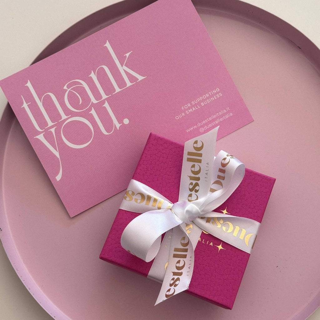 Pink gift box with white ribbon and 'thank you' card on a pink surface